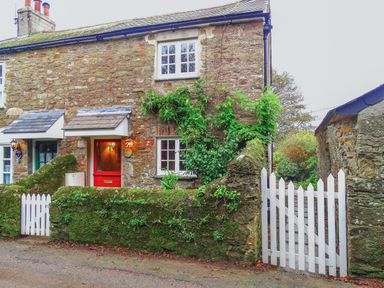 A stone cottage with a red door white window frames and a white picket gate covered with greenery at 1 Gabberwell Cottages in Kingston