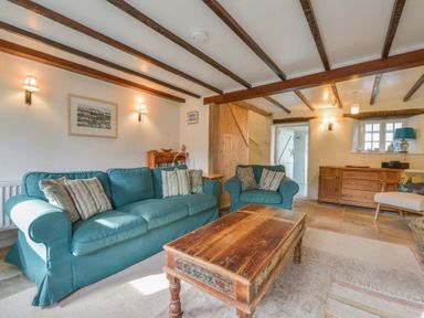 A living room with blue sofas a wooden coffee table and wooden beams on the ceiling at 1 Gabberwell Cottages in Kingston
