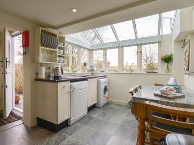 A kitchen with a dishwasher washing machine dining table and large windows showing outside at 1 Gabberwell Cottages Kingston