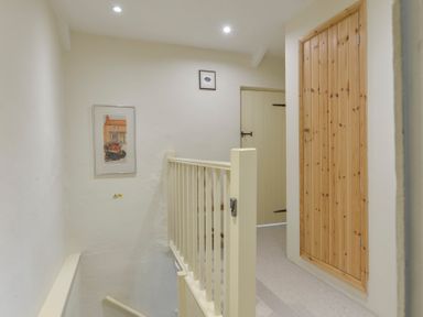 A hallway with a staircase railing two framed pictures two doors and a wooden cupboard door at 1 Gabberwell Cottages in Kingston