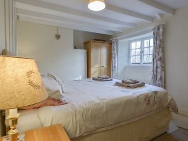 A bedroom with a bed a wooden wardrobe a window with curtains and a lamp on a bedside table at 1 Gabberwell Cottages Kingston