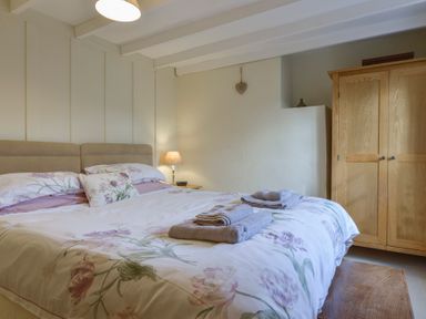 A bedroom with a bed floral bedding bedside table with lamp and wooden wardrobe at 1 Gabberwell Cottages Kingston