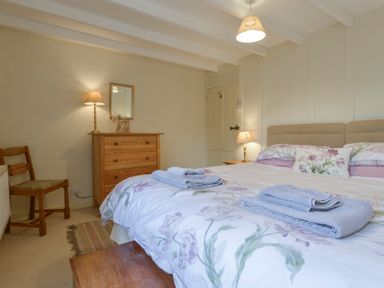 A bedroom with a bed with floral bedding and folded towels a wooden chest of drawers a wooden chair and lamps at 1 Gabberwell Cottages in Kingston