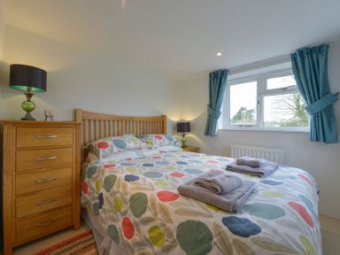 A bedroom with a wooden bed, multicolored bedding, two bedside tables with lamps, a chest of drawers, blue curtains on a window at 1 Gabberwell Cottages in Kingston