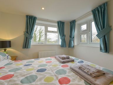 A bedroom with a bed near windows with blue curtains two towels on the bed and a lamp on a bedside table at 1 Gabberwell Cottages in Kingston