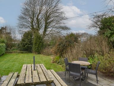A garden with a wooden picnic table and four wicker chairs around a round table at 1 Gabberwell Cottages in Kingston