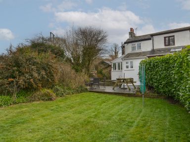 A backyard with a lawn, patio furniture, and a hedge next to a white house at 1 Gabberwell Cottages in Kingston