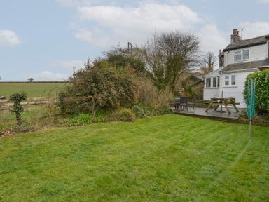 A backyard with green grass a wooden deck with outdoor furniture and a house in the background at 1 Gabberwell Cottages in Kingston