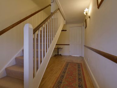 A hallway with carpeted stairs a small table a rug on wooden floor and a closed white door at Yellowland Farm in Holsworthy