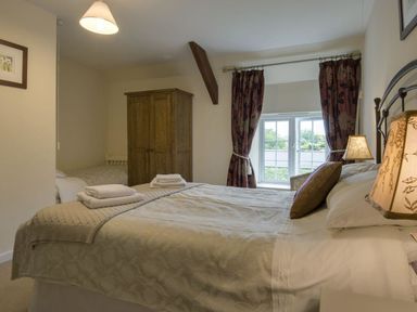 A bedroom with a double bed, bedside lamps, a wooden wardrobe, and a window with dark patterned curtains at Yellowland Farm in Holsworthy