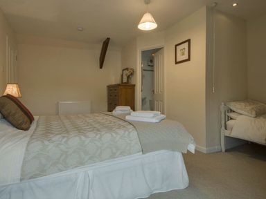 A bedroom with a double bed and folded towels wooden dresser a door leading to a bathroom and a single bed at Yellowland Farm in Holsworthy