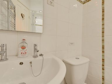 A bathroom with a white sink and chrome taps with a soap dispenser and a white toilet with tiled walls and a mirror at Yellowland Farm in Holsworthy