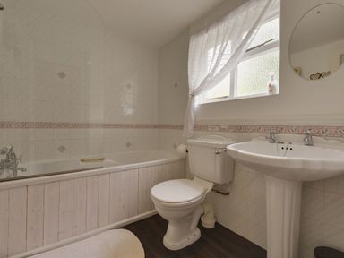 A bathroom with a bathtub toilet pedestal sink and a window with sheer curtains at Yellowland Farm in Holsworthy