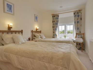 A bedroom with two single beds and a window with curtains at Yellowland Farm in Holsworthy