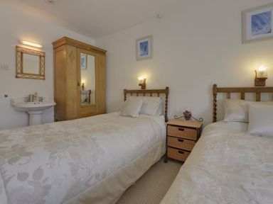 A bedroom with two single beds a wooden wardrobe a small wicker drawer unit a sink and a mirror at Yellowland Farm in Holsworthy