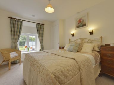 A bedroom with a bed a chair with towels a window with curtains and a painting on the wall at Yellowland Farm in Holsworthy