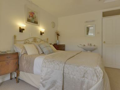 A bedroom with a bed and bedside tables next to a sink and a door at Yellowland Farm in Holsworthy