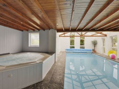 An indoor pool and hot tub with wooden ceiling and windows at Yellowland Farm in Holsworthy