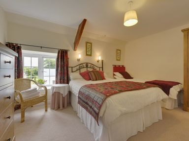A bedroom with two beds a wicker chair a small round table and a window at Yellowland Farm in Holsworthy