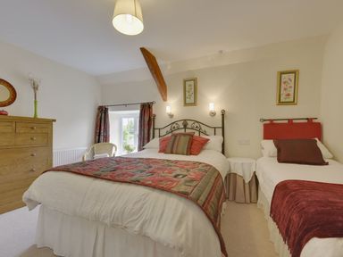 A bedroom with a double bed and a single bed a wooden chest of drawers and a wicker chair at Yellowland Farm in Holsworthy