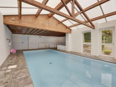 An indoor swimming pool with stone tile flooring and wooden beam ceiling at Yellowland Farm in Holsworthy