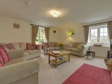 A living room with three sofas a wooden coffee table a floor lamp and windows with curtains at Yellowland Farm in Holsworthy