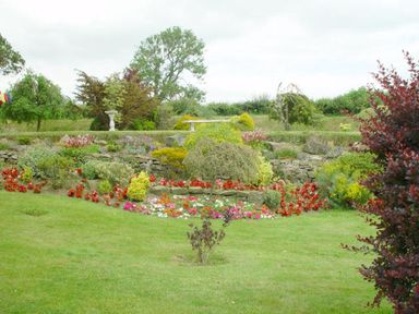 A garden with a flower bed and shrubs in front of a stone wall at Yellowland Farm in Holsworthy