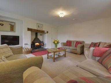 A living room with sofas a wooden coffee table a TV and a lit fireplace at Yellowland Farm in Holsworthy