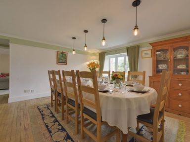 A dining room with a long table set with dishes and flowers surrounded by wooden chairs with a cabinet against the wall at Yellowland Farm in Holsworthy