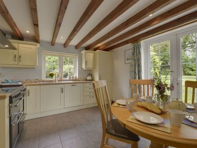 A kitchen with wooden beams on the ceiling a dining table set with plates cups and a vase with flowers near glass doors at Yellowland Farm in Holsworthy
