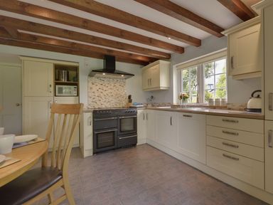 A kitchen with wooden beams on the ceiling a black stove cream cabinets a microwave on a shelf and a table with chairs at Yellowland Farm in Holsworthy