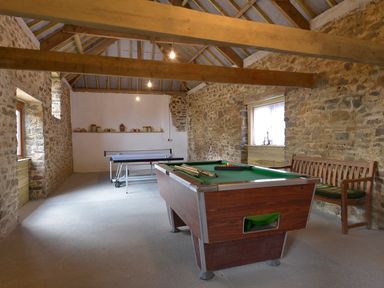 A game room with a pool table and ping pong table in a stone-walled room with wooden beams at Yellowland Farm in Holsworthy