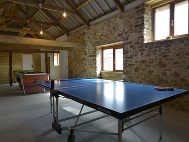 A recreational room with a ping pong table and a pool table against stone walls and wooden beams at Yellowland Farm in Holsworthy