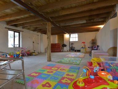 A playroom with colorful foam mats toys and small bikes under a wooden beamed ceiling at Yellowland Farm in Holsworthy