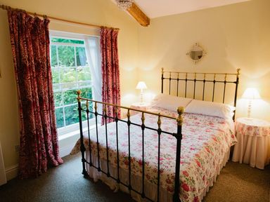 A bedroom with a metal bed frame and floral bedspread next to a window with patterned curtains at Parnacott in Holsworthy