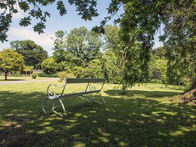 A metal bench on grass under trees in a garden at Parnacott in Holsworthy