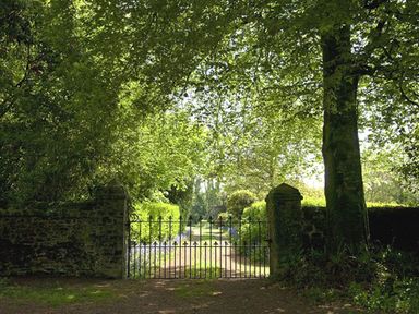 An iron gate on a gravel path surrounded by stone pillars and dense green trees at Parnacott in Holsworthy