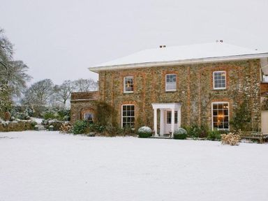 A large brick house with a white porch in a snowy yard with bare trees at Parnacott in Holsworthy