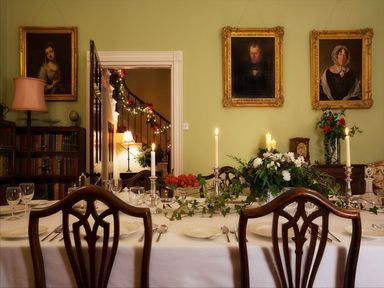 A dining room with a long table set with candles flowers and plates portraits on walls at Parnacott in Holsworthy