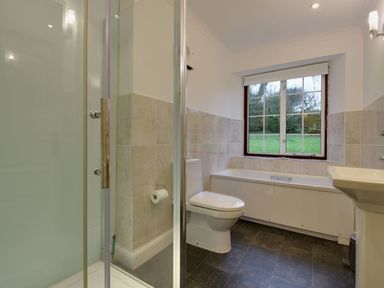 A bathroom with a shower, toilet, bathtub, and sink with a window showing greenery outside at Higher Tumrose in Blisland
