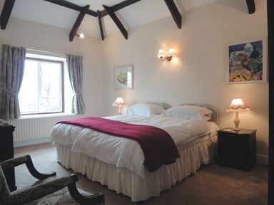 A bedroom with a double bed a red throw on the bed bedside tables with lamps a window and exposed ceiling beams at Higher Tumrose in Blisland