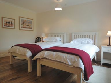 A bedroom with two single beds with red throws white bedding bedside tables and lamps at Higher Tumrose in Blisland