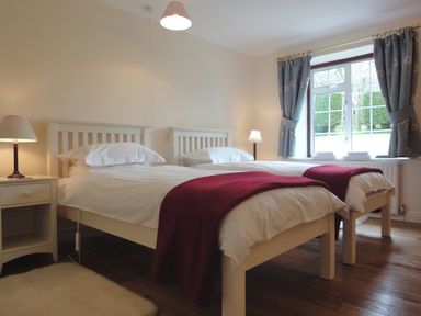 A bedroom with two single beds two bedside tables with lamps and a window with curtains at Higher Tumrose in Blisland
