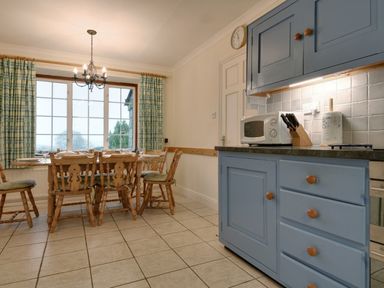 A kitchen with blue cabinets wooden dining table and chairs and a chandelier at Higher Tumrose in Blisland