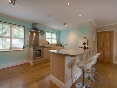 A kitchen with a countertop and bar stools near a wooden door at Grandpa Dickson's in Little Petherick