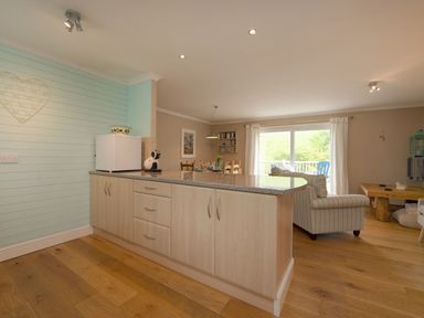 A kitchen island with a white mini fridge and coffee machine overlooking a dining table and living area at Grandpa Dickson's in Little Petherick