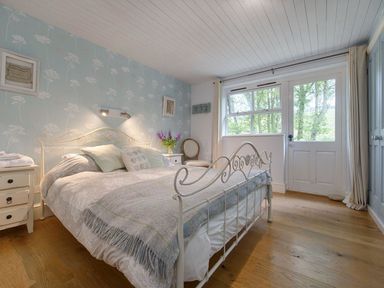 A bedroom with a double bed bedside tables a window and a door at Grandpa Dicksons in Little Petherick