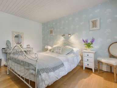 A bedroom with a metal bed frame bedside tables flowers a chair and a dressing table at Grandpa Dicksons in Little Petherick
