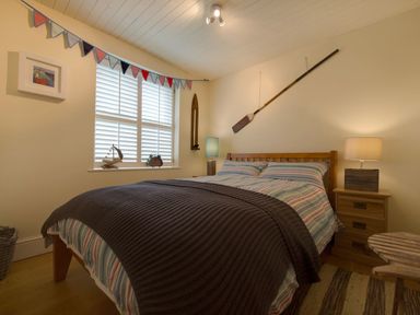 A bedroom with a wooden bed striped bedding two bedside tables lamps a window with shutters and nautical decorations at Grandpa Dickson's in Little Petherick
