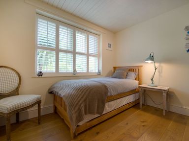 A bedroom with a single wooden bed a bedside table with a lamp a chair and a window with shutters at Grandpa Dickson's in Little Petherick